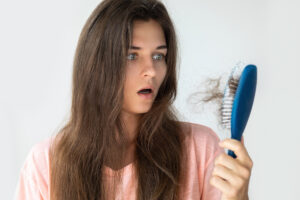 Woman looking in horror at a large clump of hair attached to her hair brush.